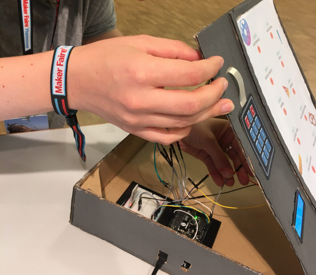 Eine Hand öffnet einen selbstgebauten Prototypen. Im Inneren offenbaren sich viele Kabel und ein Mikrocontroller.