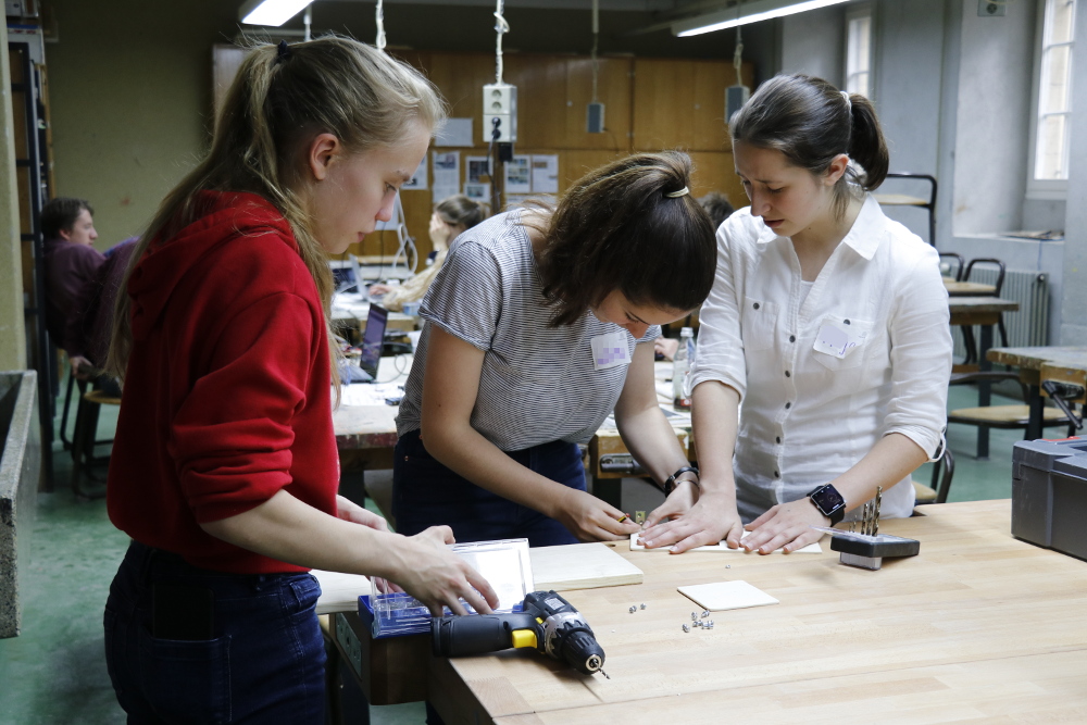 Drei Mädchen arbeiten mit Holz und Bohrmaschine.