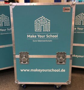 Zu sehen ist eine hüfthohe hellblaue Box mit zwei Schnellverschlüssen an der Vorderseite und Rollen für den Transport. Auf der Box ist das Make Your School Logo aufgeklebt.