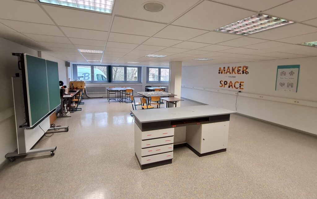 In einem Klassenraum stehen Tische. An der Wand ist ein Logo mit dem Schriftzug "Maker Space" zu sehen. 