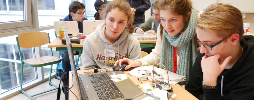 Eine Mentorin hilft einem Schüler und einer Schülerin beim Programmieren.