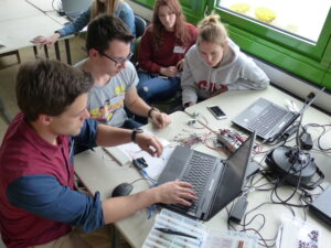 Eine Gruppe von Jugendlichen sitzt um einen Laptop und schaut auf dessen Bildschirm.