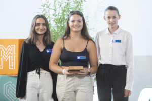 Drei Mädchen lachen in die Kamera und halten den Make-Your-School-Award in den Händen.