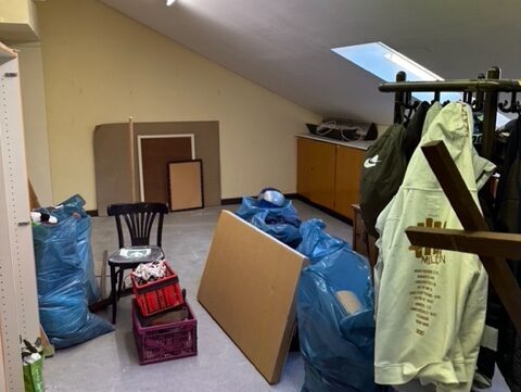 Ein Raum mit schräger Decke ist vollgestellt mit Stühlen, Tischen, Schränken, einer Garderobe.