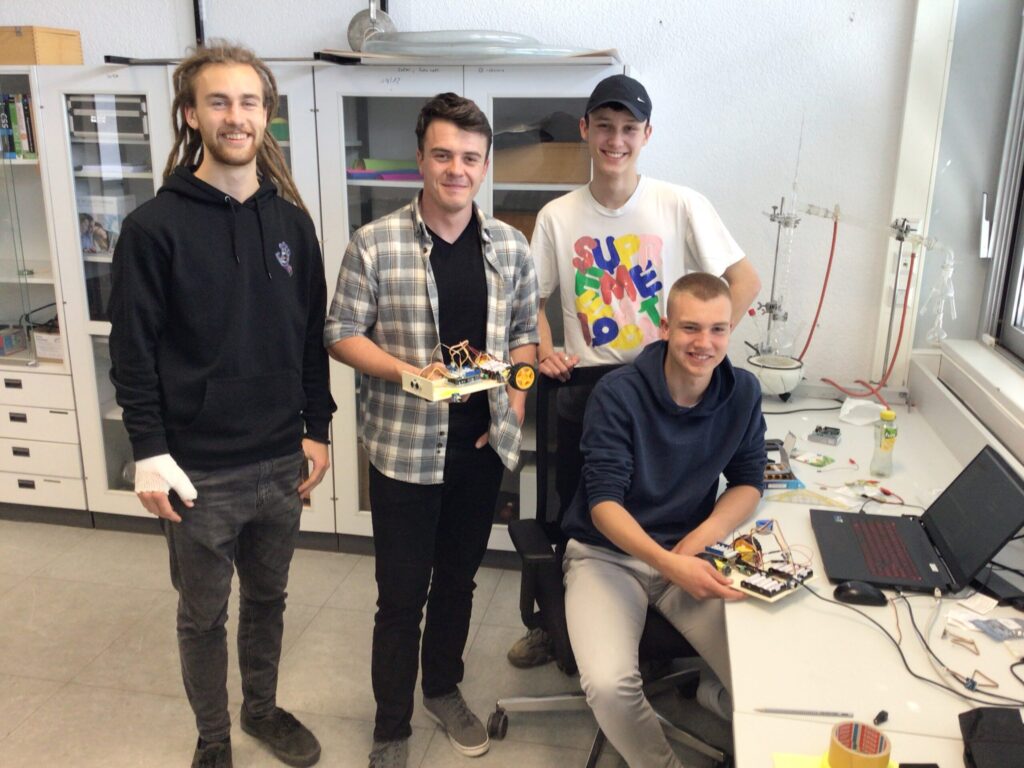 Vier Jungs stehen für ein Gruppenbild zusammen und lachen. Einer hält den Prototypen des Roboters in der Hand.