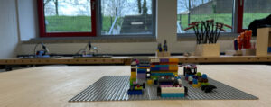 Auf einem Werktisch steht das Legomodell eines Raumes. Im Hintergrund stehen Werkzeuge.