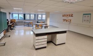 In einem Klassenraum stehen Tische. An der Wand ist ein Logo mit dem Schriftzug "Maker Space" zu sehen.