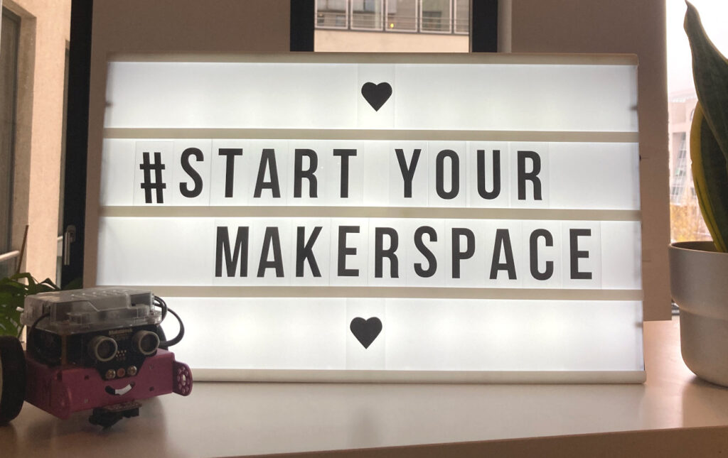 Auf einer Lightbox steht: Start Your Makerspace. Daneben steht ein kleiner fahrbarer Roboter.