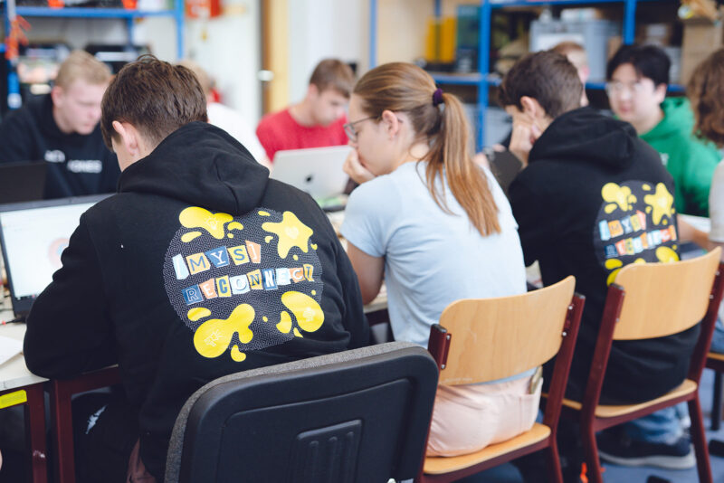 Jugendliche sitzen an einem langen Tisch und schauen konzentriert.