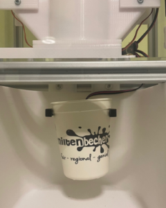 To-Go-Becher mit dem Logo "Milten Becher" unter einem Automaten