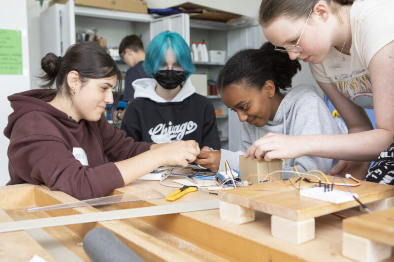 Vier Schülerinnen sitzen um einen Tisch und stecken konzentriert technische Bauteile zusammen