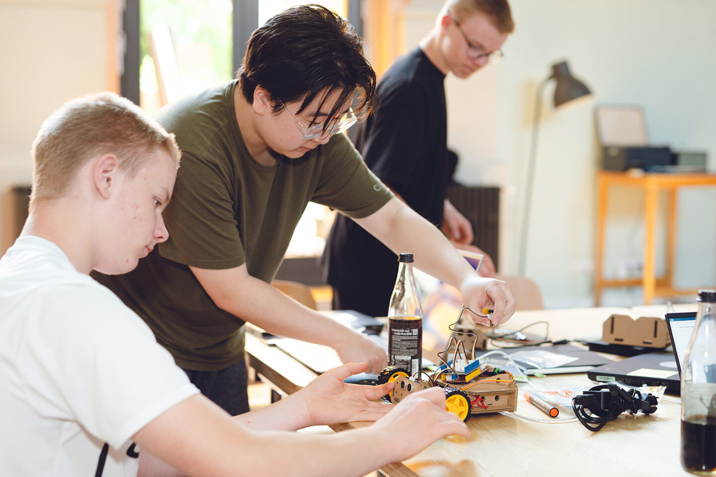 Zwei männlich gelesene Jugendliche tüfteln an einem Roboter am Tisch.