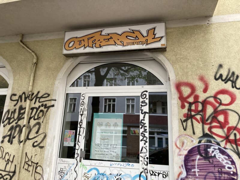 Eingang eines Jugendzentrums: Über dem Eingang steht "Outreach Berlin", am Eingangfenster ist ein Plakat von Make Your School. Die Wände drum herum sind mit Graffiti gesprüht.