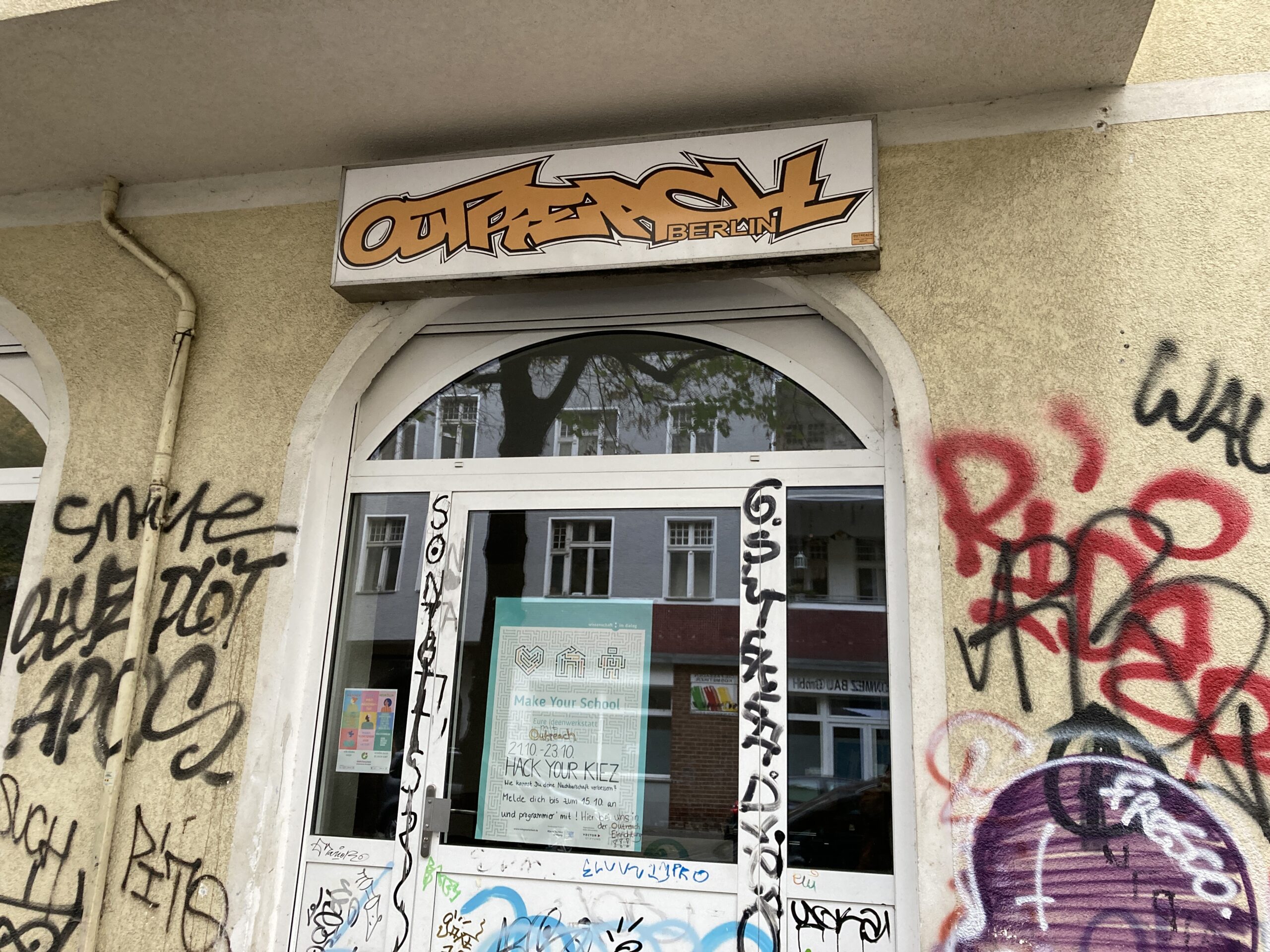 Eingang eines Jugendzentrums: Über dem Eingang steht "Outreach Berlin", am Eingangfenster ist ein Plakat von Make Your School. Die Wände drum herum sind mit Graffiti gesprüht.