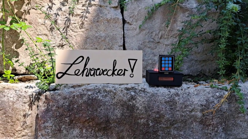 Ein Prototyp mit Tastenfeld und LCD-Bildschirm, daneben das Schild mit Aufschrift "Lehrerwecker"