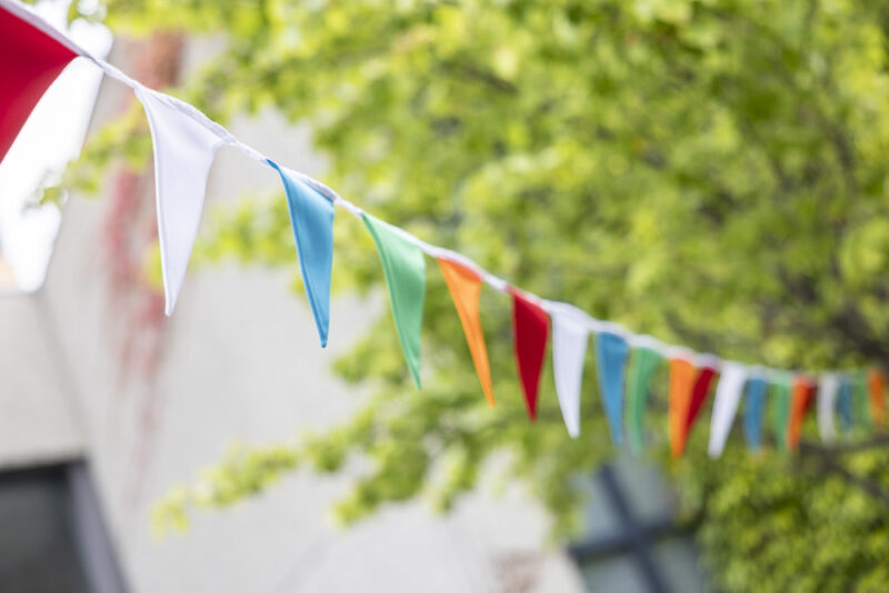Eine bunte Wimpelkette hängt vor dem Hintergrund von Bäumen.